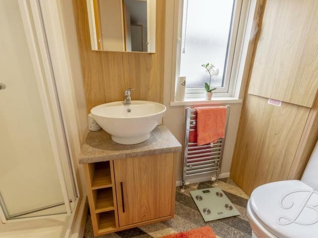 Our last image from the interior of the mobile home focuses on the family shower room. A three-piece suite comprises a shower cubicle, hand wash basin and low-flush WC, plus a cupboard for additional storage.