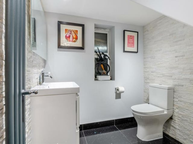 The downstairs cloakroom is made up of a modern two-piece suite that comprises a low-flush WC and wash hand basin with storage drawers beneath. Automatic LED lighting means three spotlights switch on as soon as you enter, while the floor is quartz-tiled and there is a feature quartz-tiled wall behind the sink with a fitted mirror.