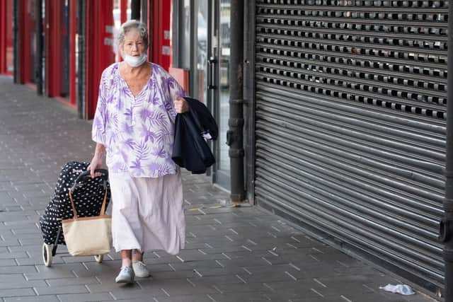 A woman wearing a surgical face mask walks passed closed shops (Photo by Matthew Horwood/Getty Images)
