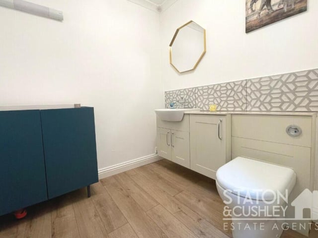 The ground floor also houses this toilet with low-level WC, vanity unit with sink and mixer tap, laminate flooring and tiled splashbacks..
