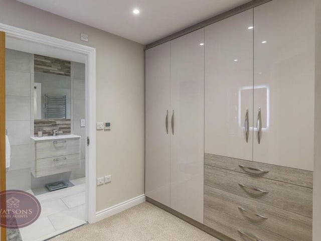 The master bedroom opens into this smart dressing room, which has fitted wardrobes and a dressing table, a built-in vanity mirror with lighting, ceiling spotlights and an oak door to the en suite.