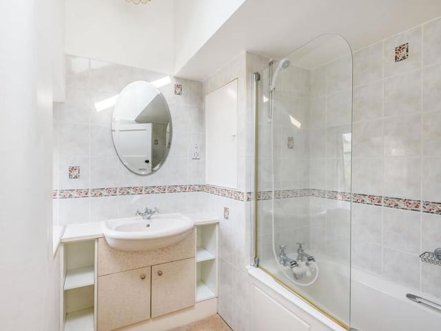 Our last image from the interior focuses on the family bathroom, which has a panelled bath with shower over. There is also a vanity unit with inset wash hand basin and storage cupboard and shelving beneath.