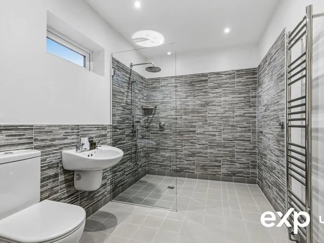 Comprising a modern suite, the luxury family bathroom consists a p-shaped bath with shower over, a washbasin in a vanity unit, and a low-flush w.c. This room is decorated with part-tiled walls. There is a heated towel rail and a window to the side.