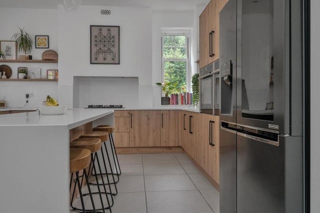 The kitchen features two integrated Neff ovens and a five-ring Neff gas hob with extractor hood above. A breakfast island has matching base units, drawers and white quartz worktops, with space for stools at one side and three light points directly above.