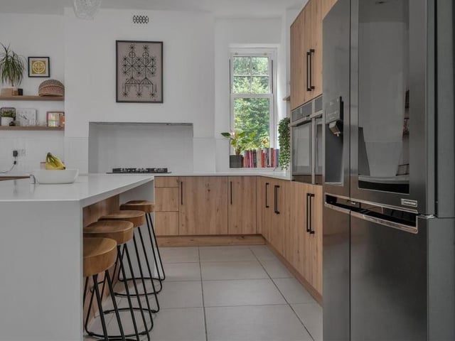 The kitchen features two integrated Neff ovens and a five-ring Neff gas hob with extractor hood above. A breakfast island has matching base units, drawers and white quartz worktops, with space for stools at one side and three light points directly above.