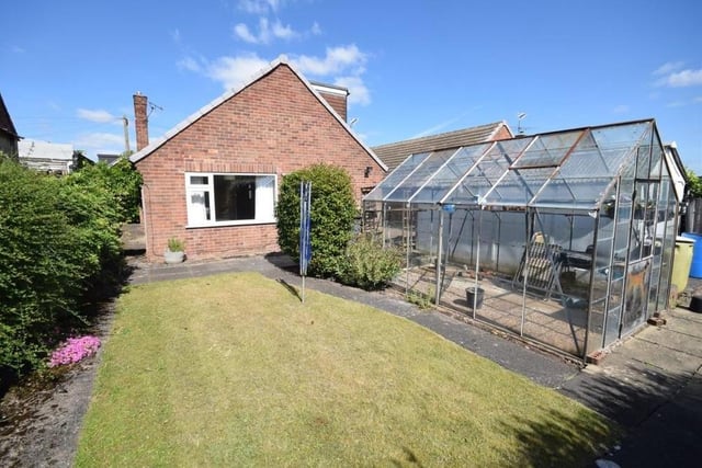 This is the view from the back of the dormer bungalow, showing a garden that is mainly laid to lawn but also includes a wide array of mature shrubs and flowers, with a patio seating area. The green-fingered among you will also be excited to notice a large greenhouse.