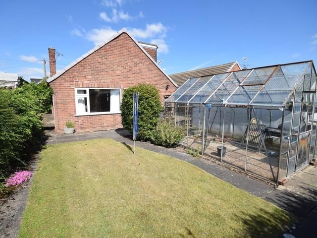 This is the view from the back of the dormer bungalow, showing a garden that is mainly laid to lawn but also includes a wide array of mature shrubs and flowers, with a patio seating area. The green-fingered among you will also be excited to notice a large greenhouse.