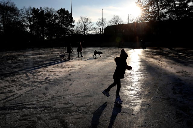 People skate and walk their dogs on a frozen pond at Victoria Park in Glasgow