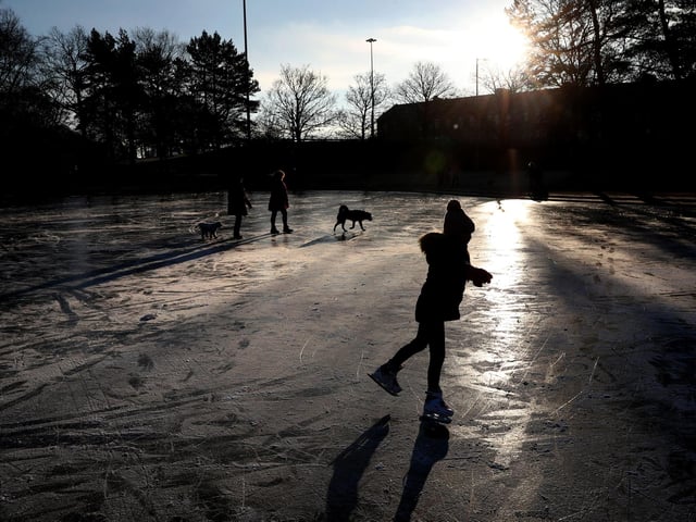 People skate and walk their dogs on a frozen pond at Victoria Park in Glasgow