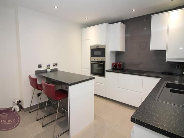 The kitchen features a breakfast bar, ceiling spotlights and a range of matching wall and base units. Work surfaces incorporate an inset one-and-a-half-bowl sink and drainer unit.