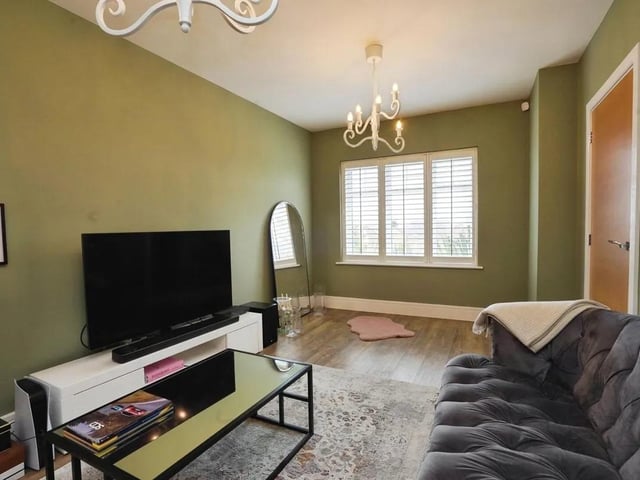 This elegant sitting room is characterised by its muted green walls and warm wooden flooring, with amtico flooring and a window.