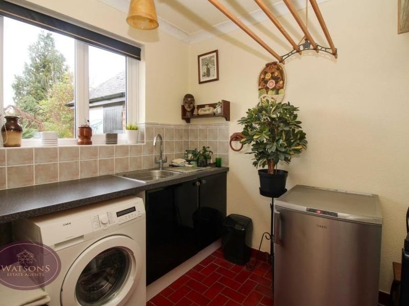 Across an inner hallway from the kitchen sits this handy utility room. It has a stainless steel sink and drainer unit, tiled flooring, space and plumbing for a washing machine and even access to the property's attic.