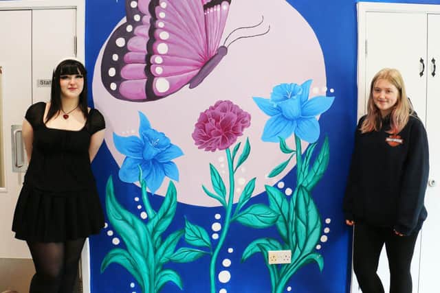 Lexi Snood (left) and Caitlyn Stinson (right) proudly stand by the butterfly moon mural in Rumbles C