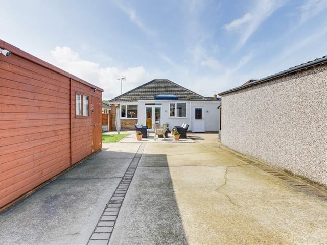 Let's take a look outside the £260,000 bungalow now, starting with this view from the rear. A patio pathway sits between one of two large, timber-built garden sheds to the left and a garage, with up-and-over door, to the right.