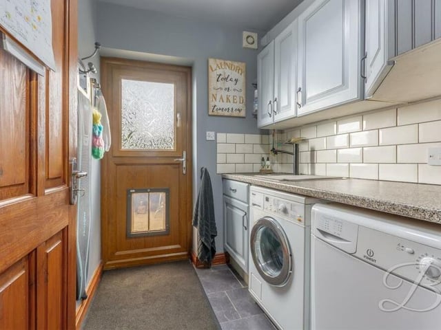 Just off the kitchen is this convenient utility room, which boasts plumbing for a washing machine, a work surface and inset sink with mixer tap above. There are also cabinets for additional storage, while the door leads outside.