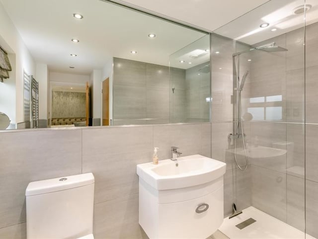 The en suite bathroom to the master bedroom can only be described as excellent. A three-piece white suite with chrome fittings consists of a walk-in, tiled shower enclosure with 'rainfall' shower and an extra handset, vanity unit with inset wash hand basin and storage drawer beneath, and a low-flush WC. Attractive, modern tiling, eight ceiling spotlights and a heated towel-rail add the finishing touches.