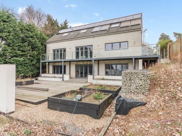 Time to step outside now, and here is a view of the rear of the property, showing the wraparound balcony, rooftop solar panels and large, decked patio.