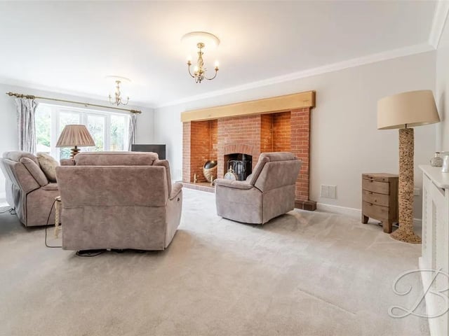 The living room offers a warm and inviting space with soft carpeted flooring, a striking exposed brick feature fireplace, and double doors that open out to the garden, creating a perfect blend of comfort and indoor-outdoor living.