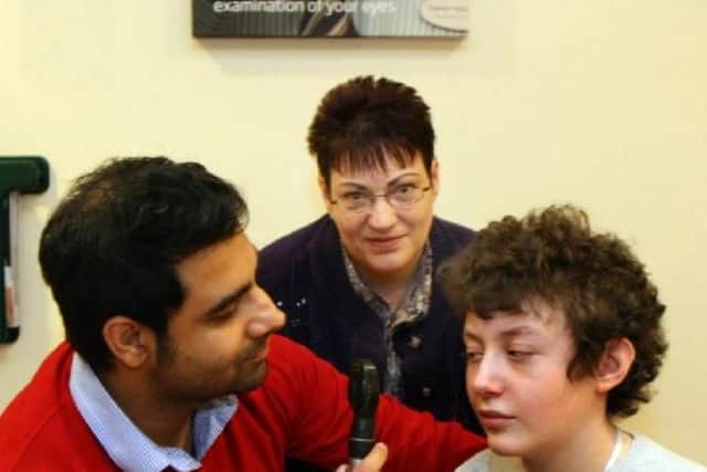 Optometrist Sunny Boyal uses a Ophthalmscope to see into James Morley's eye in 2014, looking on is James mother Pam.