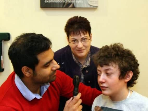 Optometrist Sunny Boyal uses a Ophthalmscope to see into James Morley's eye in 2014, looking on is James mother Pam.