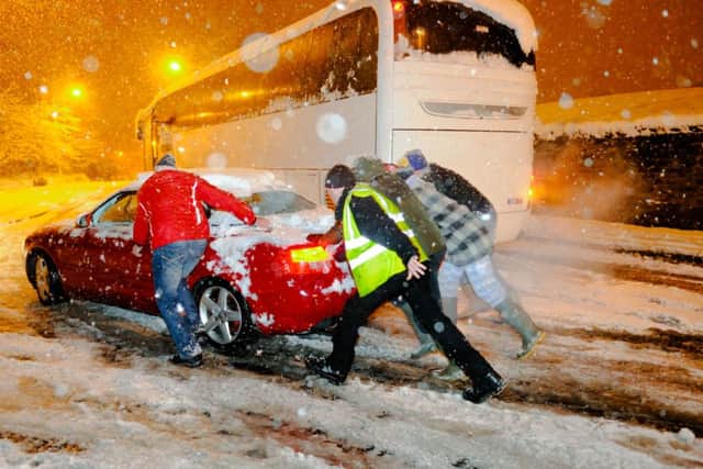 Several people help to push a car pass an abandoned coach as severe snow storm hits Mansfield Woodhouse in the East Midlands, England