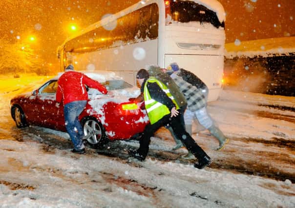 Several people help to push a car pass an abandoned coach as severe snow storm hits Mansfield Woodhouse in the East Midlands, England