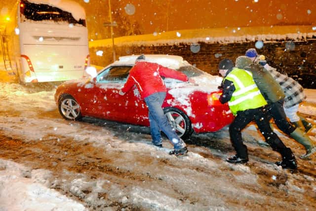 Several people help to push a car pass an abandoned coach as severe snow storm hits Mansfield Woodhouse