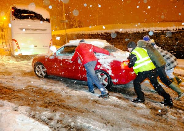 Several people help to push a car pass an abandoned coach as severe snow storm hits Mansfield Woodhouse
