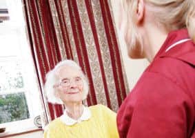 A young pregnant carer sits drinking a cup of tea with her elderly home care pacient