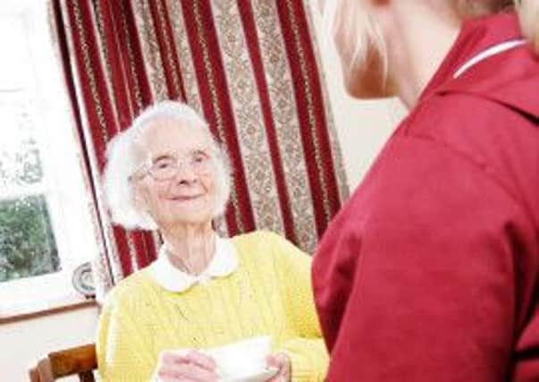 A young pregnant carer sits drinking a cup of tea with her elderly home care pacient