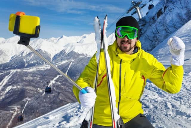Man taking a selfie with stick and lifted hand over the mountain and cablecar ski lift with cabins