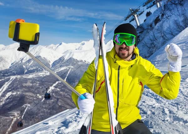 Man taking a selfie with stick and lifted hand over the mountain and cablecar ski lift with cabins
